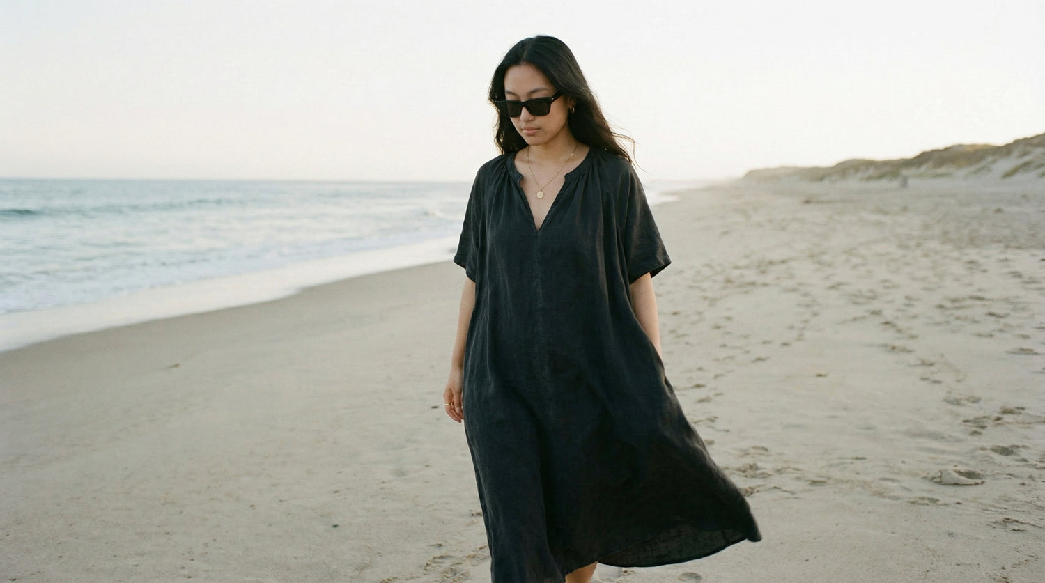 Woman in a dark dress standing on a beach with ocean in the background
