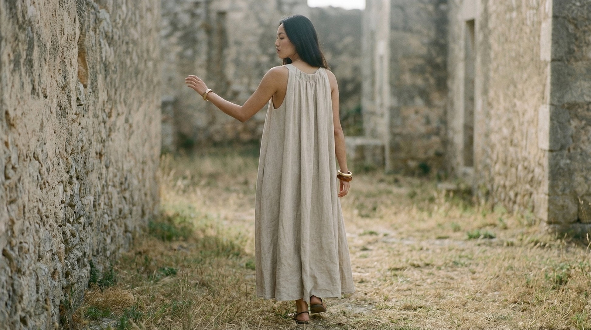 Woman in a beige dress standing in an old stone building ruin.